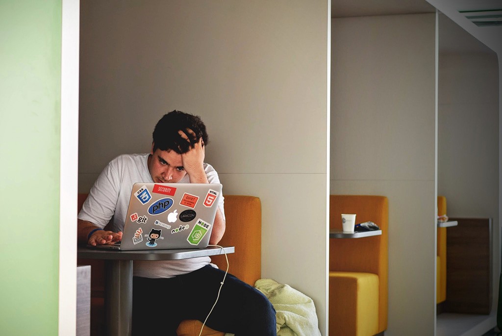 Mann sitzt vor einem MacBook und arbeitet. Mit der Hand stützt er seinen Kopf.