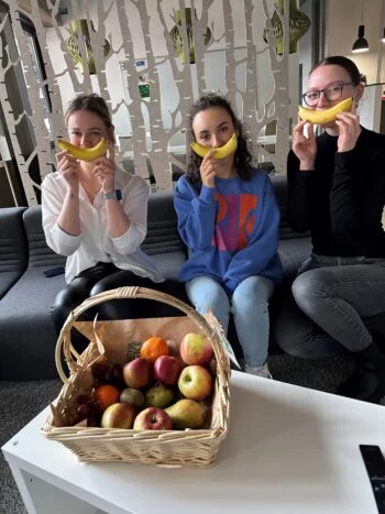 Drei Mitarbeiterinnen sitzen auf einem Sofa mit einem Obstkorb