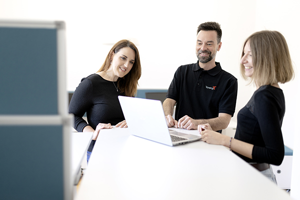 Drei Personen lächeln während sie auf einen Laptop schauen