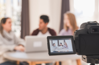 Eine Videokamera filmt drei Personen vor einem Laptop